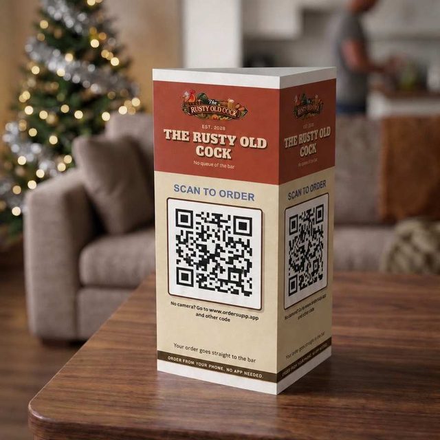 A printed table talker on a coffee table, a Christmas tree behind it: the pub's name and a Scan to order code